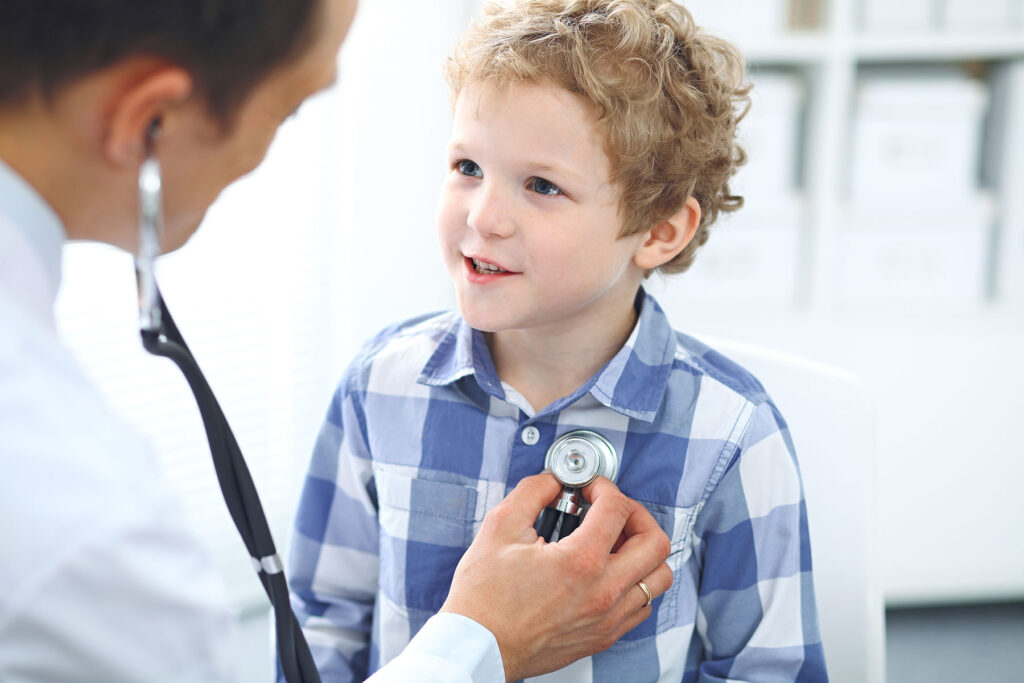 A doctor listening to a smiling child's heart beat with their stethoscope.
