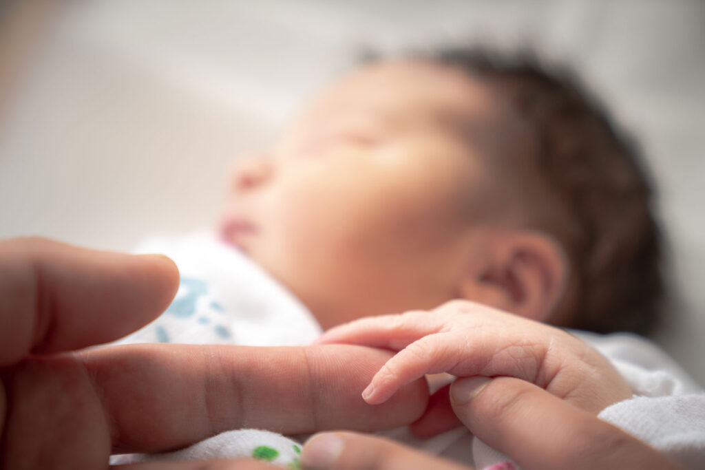 A newborn baby touching holding an adults finger.