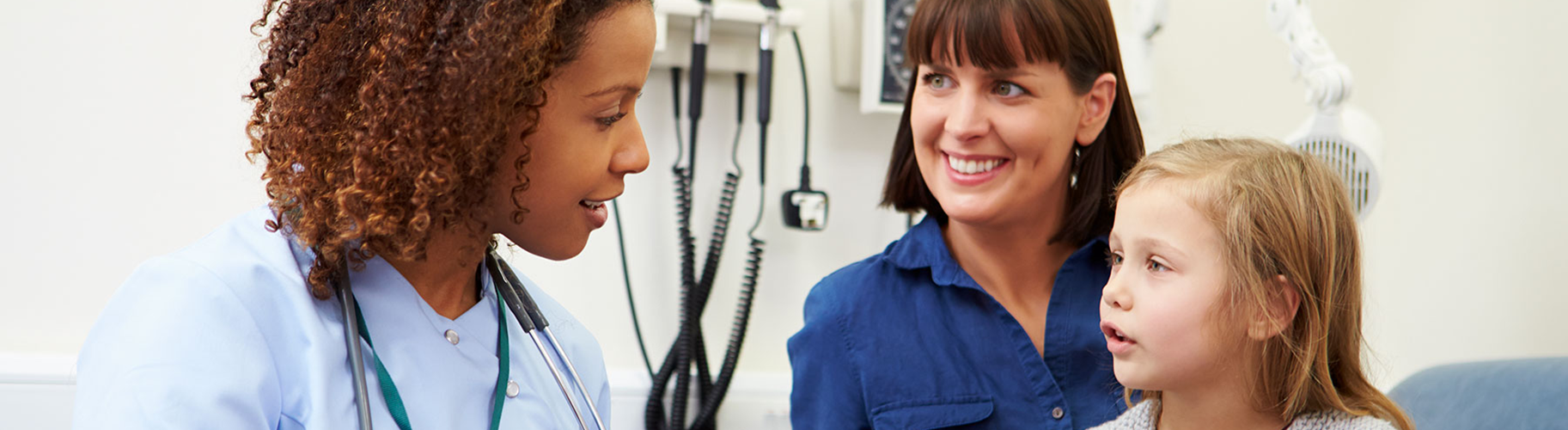 A doctor speaking to a child and her mother in an exam room.