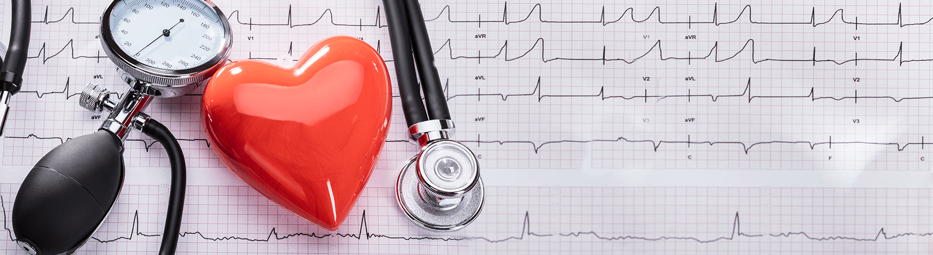 A stethoscope. the dial of a blood pressure sensor, and a shiny red heart charm sit atop a piece of graph paper with heart rate monitoring lines drawn of it.