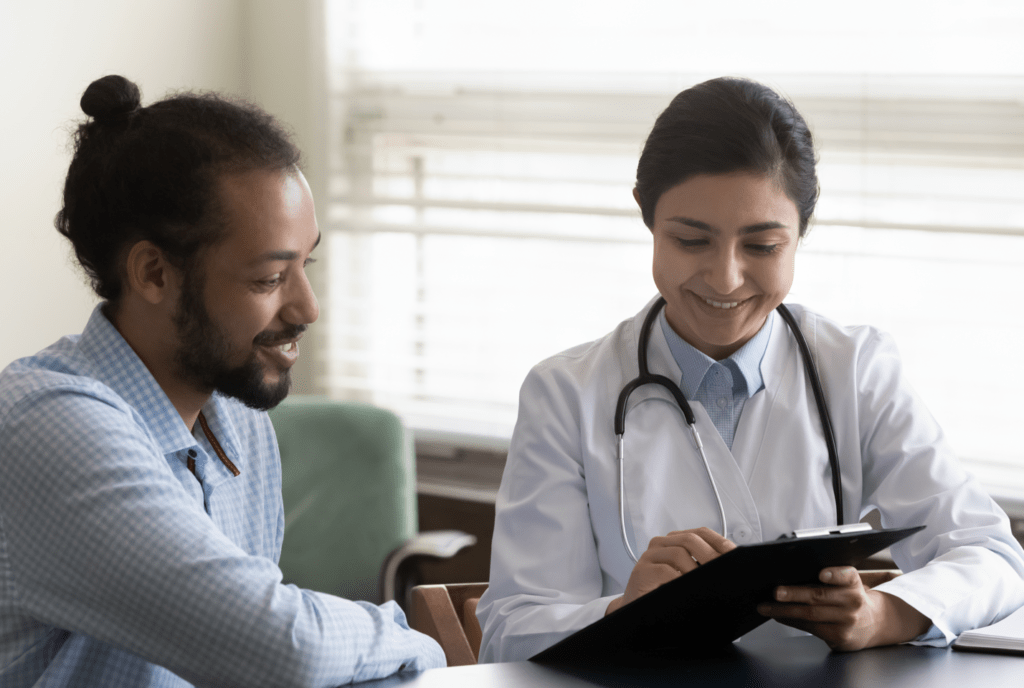 A doctor and a man looking at a clipboard together smiling.