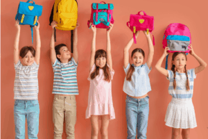 Back to school Five children in colorful clothing raise their backpacks above their heads.