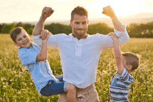 A man holding his arms up with two young boys hanging on to his biceps.