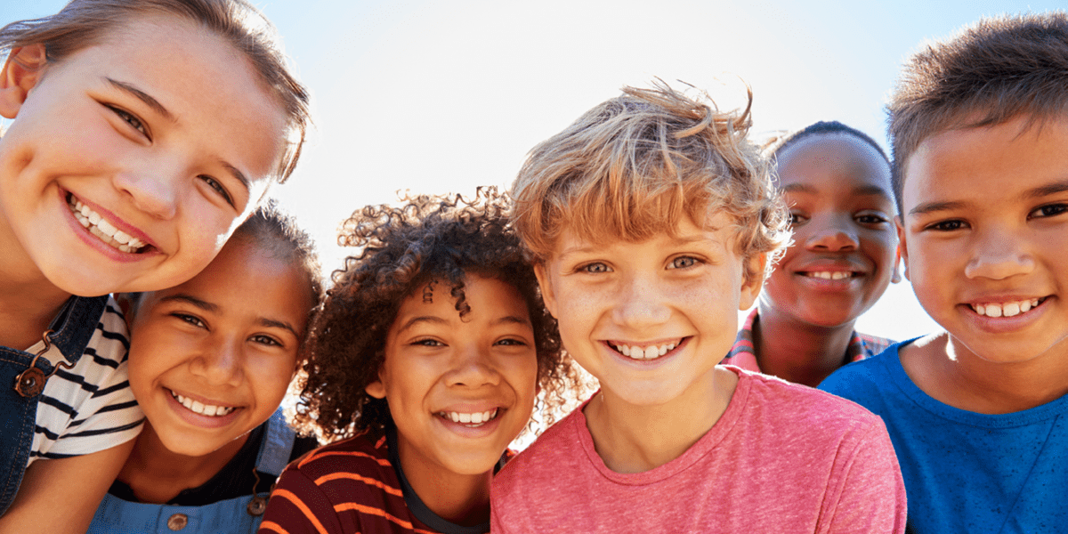 Several children from diverse backgrounds gather around smiling.