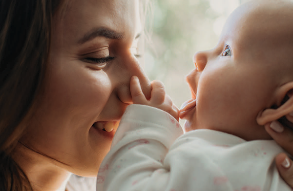 Mother and baby smiling while baby touches mothers nose.