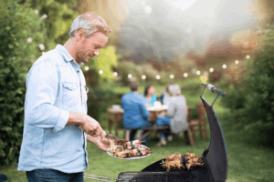 A man loads a plate with kabobs while others sit at a table in the background.