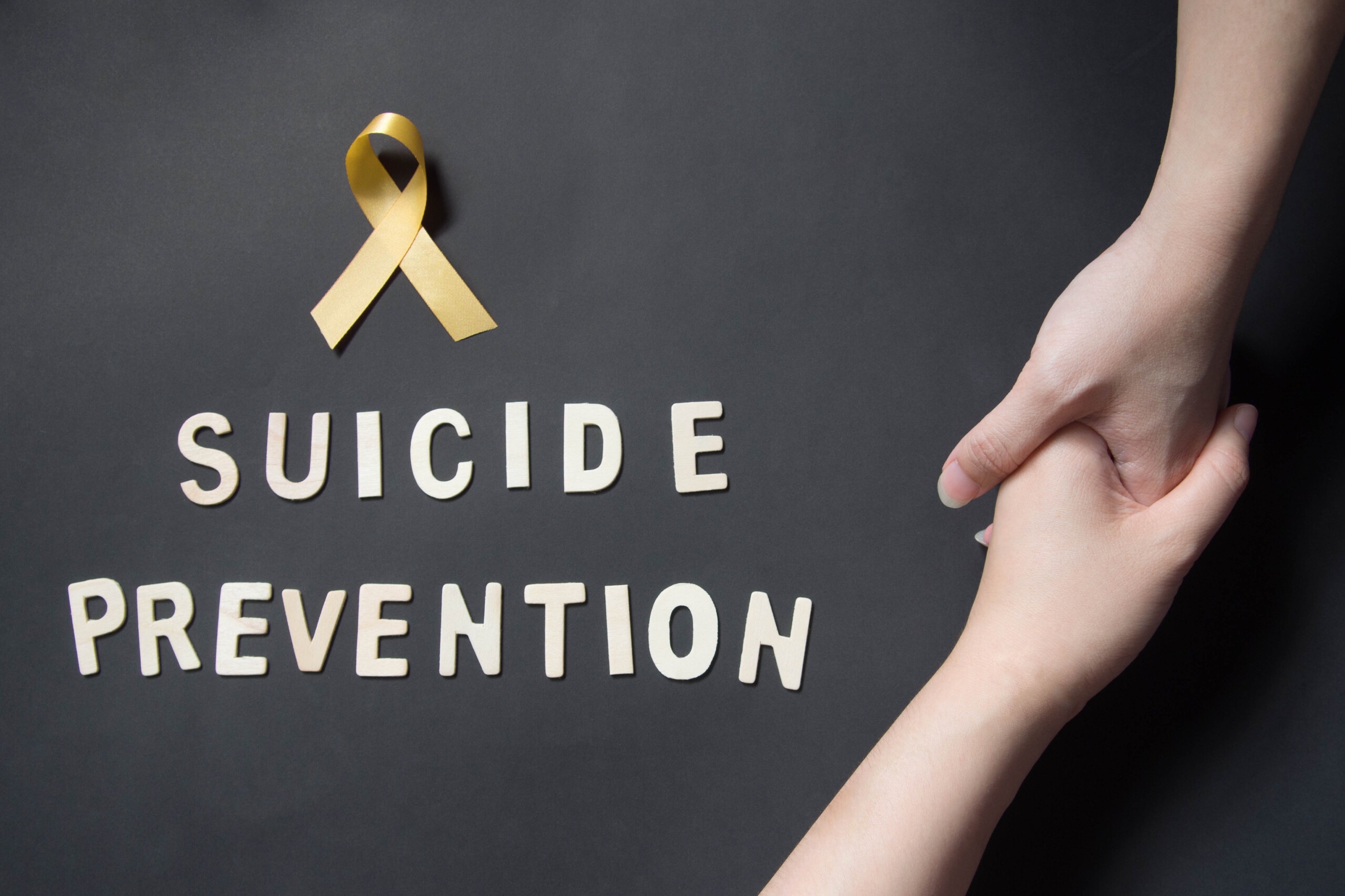 A yellow ribbon and a pair of holding hands with the words "suicide prevention".